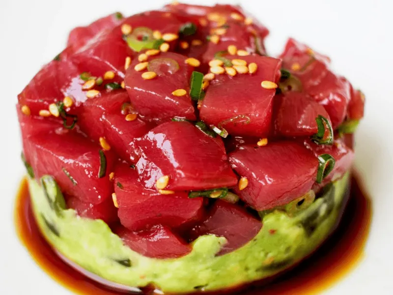Tuna tartare stacked over a layer of avocado with soy dressing pooling around the base.
