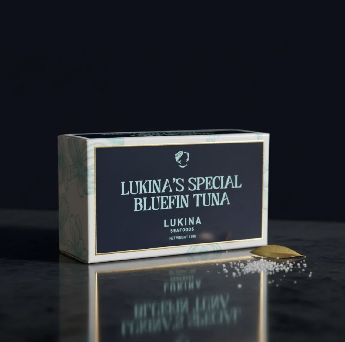 Lukina's Special Bluefin Tuna box on a dark surface with a small spoon and scattered salt crystals nearby.
