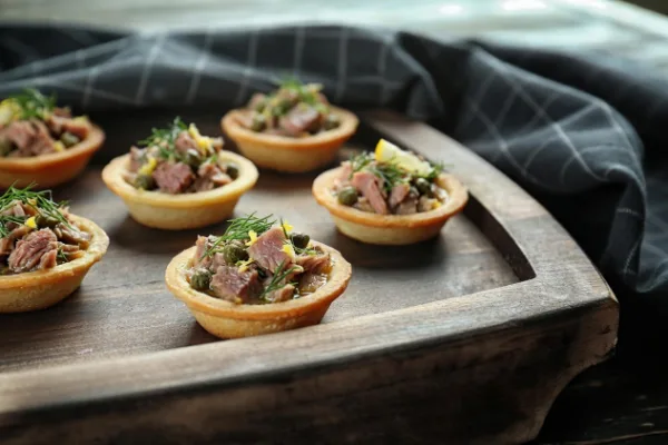 Christmas Canapes Mini Bluefin Tuna Tartlets With Lemon, Capers And Dill sitting on commercial kitchen pass.